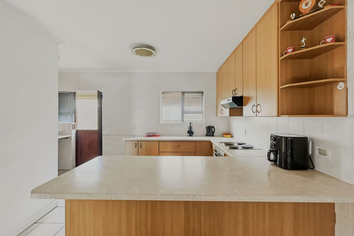 A functional kitchen featuring wooden cabinetry, laminate countertops, an electric hob with extractor fan, and a breakfast nook, with tiled flooring and backsplash.
