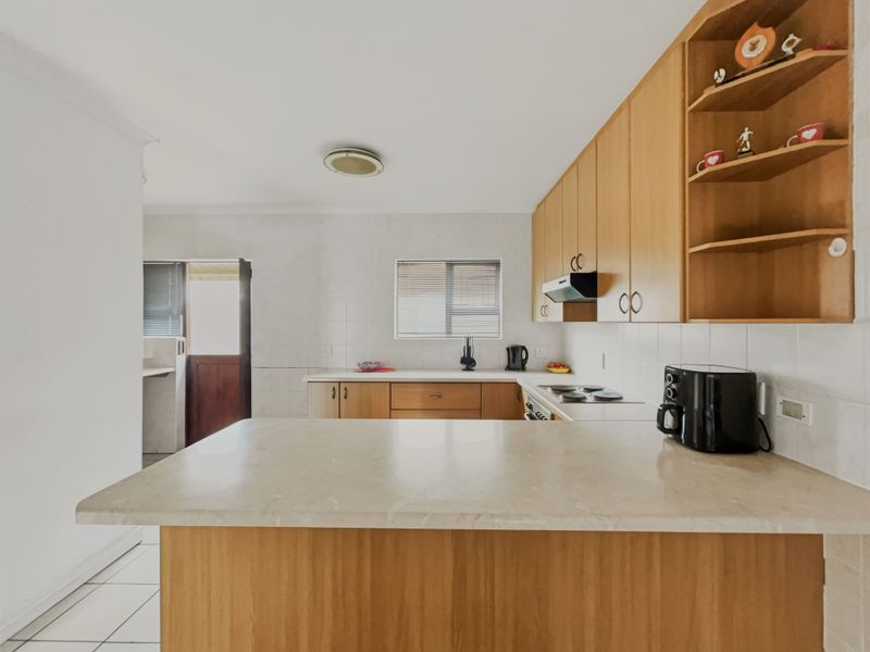 A functional kitchen featuring wooden cabinetry, laminate countertops, an electric hob with extractor fan, and a breakfast nook, with tiled flooring and backsplash.