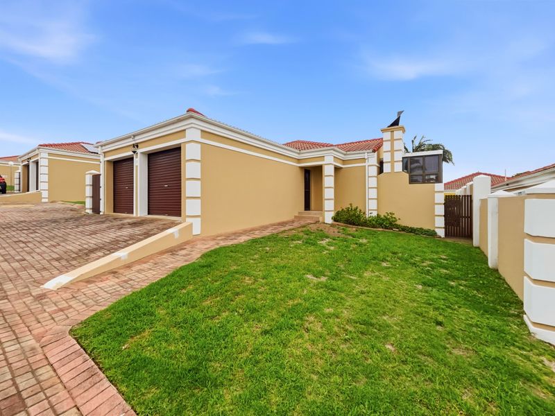 Front view of a cluster home featuring a double garage, paved driveway, well-maintained lawn, and secure boundary walling.