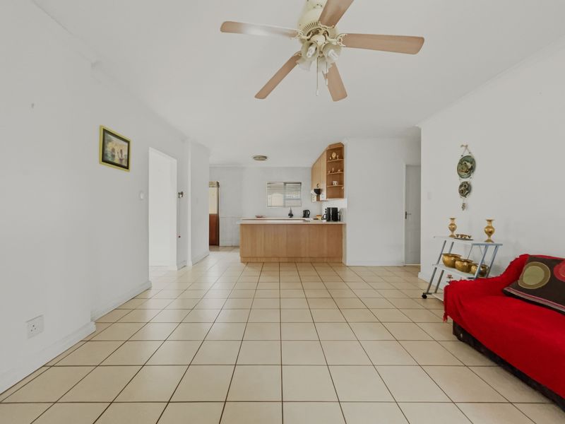 Open-plan living area featuring tiled flooring, a ceiling fan, and a functional kitchen with built-in cabinetry and a central island.