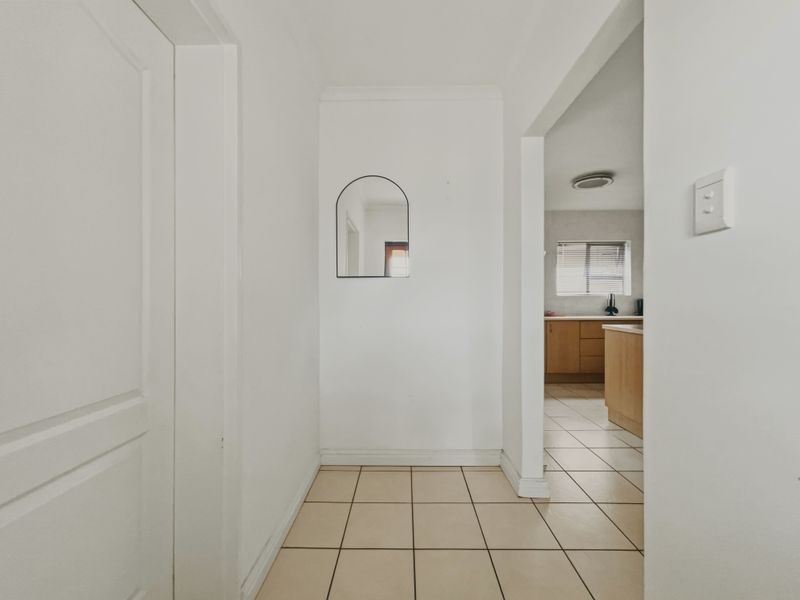 A clean, neutral hallway with tiled flooring leading into an adjacent kitchen area.