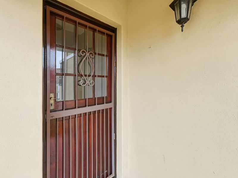 A secure entrance featuring a wooden and metal security gate with glass panels and a mounted exterior wall light.
