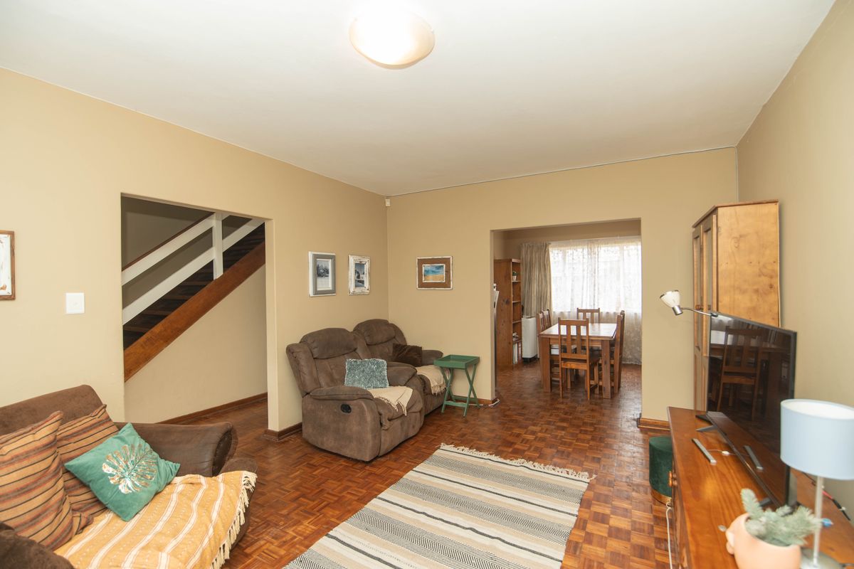 A living room featuring classic parquet flooring and an open-plan layout leading to a dining area and staircase.