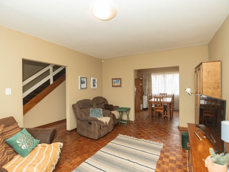 A living room featuring classic parquet flooring and an open-plan layout leading to a dining area and staircase.
