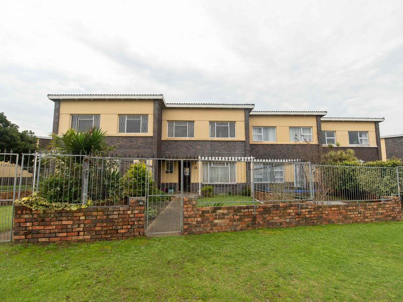 Front elevation of a multi-level townhouse featuring a brick facade, metal security fencing, and a paved entrance walkway.