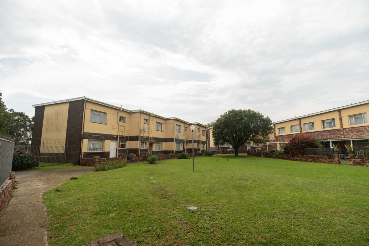 A view of the rear exterior of the townhouse complex, featuring a shared lawn area, paved walkways, and multi-story residential units.