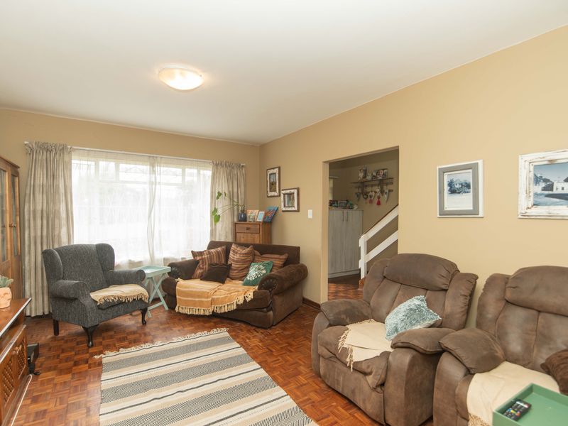 A comfortable living room featuring classic parquet flooring, neutral wall tones, and a large window allowing for natural light.