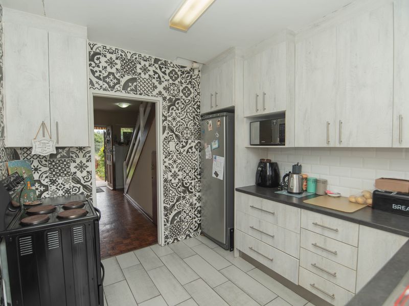 A functional kitchen featuring light wood-grain cabinetry, a striking patterned feature wall, subway tile backsplash, and ceramic floor tiles with direct access to the hallway.