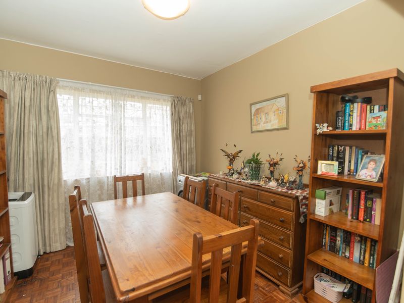 A dining room featuring parquet flooring and a large window with curtains, providing a functional space for meals.