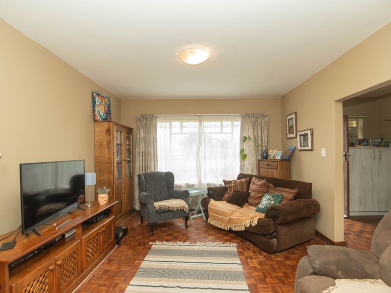 A cozy living room featuring classic parquet flooring and natural light from a large window, offering a warm and inviting atmosphere.