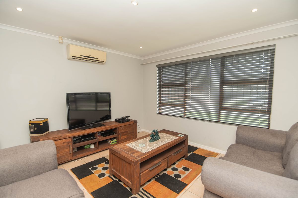 A comfortable living room featuring tiled flooring, recessed downlighting, and a wall-mounted split-system air conditioner, complemented by large windows with venetian blinds.