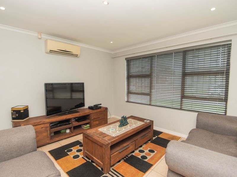 A comfortable living room featuring tiled flooring, recessed downlighting, and a wall-mounted split-system air conditioner, complemented by large windows with venetian blinds.