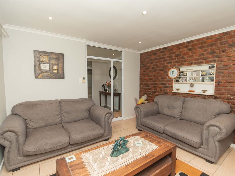 A living room featuring an exposed brick accent wall, tiled flooring, recessed lighting, and a glass-paneled door leading to an adjacent space.