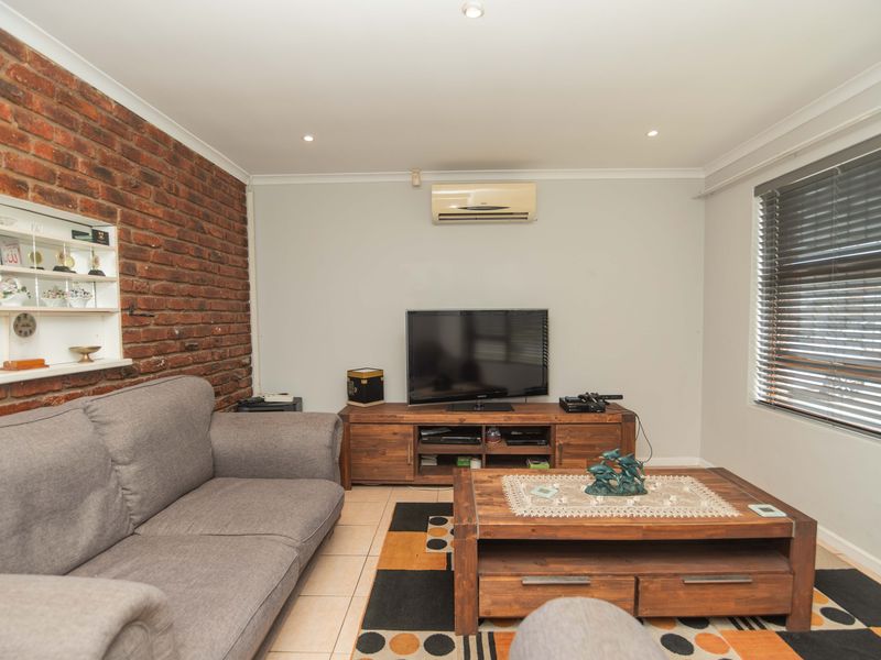 A living room featuring an exposed brick feature wall, tiled flooring, recessed lighting, and a wall-mounted split-system air conditioner.