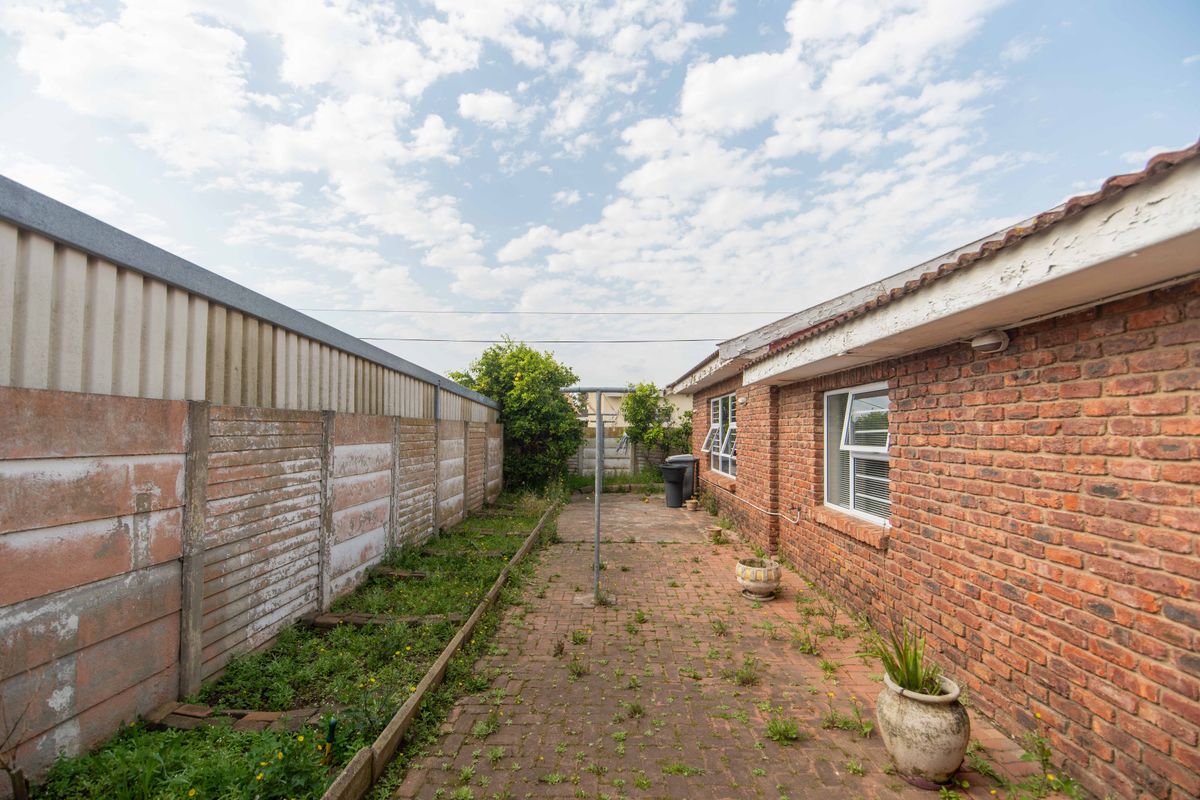 Rear exterior view of the property featuring a brick facade, paved patio area, and a precast concrete boundary wall requiring maintenance.