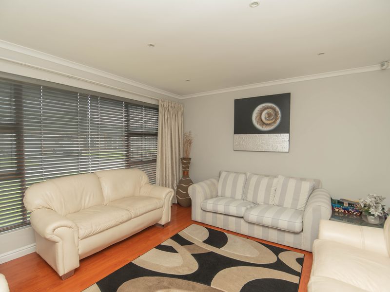 A well-lit living room featuring laminate flooring, recessed downlighting, and large windows fitted with venetian blinds.