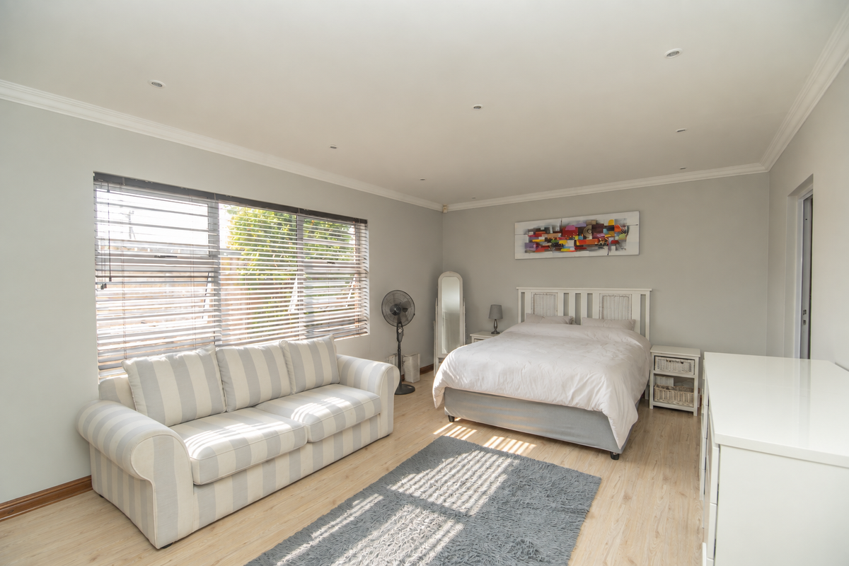 A spacious bedroom featuring light laminate flooring, recessed downlighting, and large windows fitted with venetian blinds, offering a bright and neutral living space.