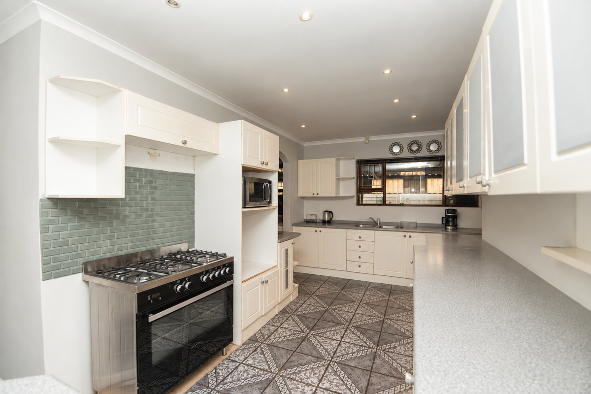 A functional kitchen featuring cream cabinetry, a gas stove with oven, a tiled backsplash, and patterned floor tiles with ample counter space.