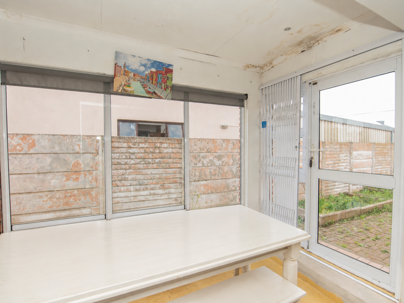 Enclosed patio area featuring exposed brickwork, large sliding windows, and direct access to the rear garden through a security-fitted door.