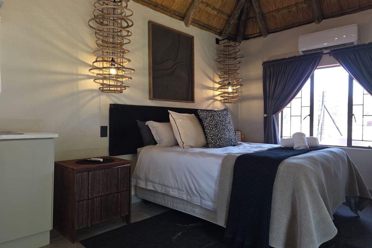 A cozy bedroom featuring a traditional thatched roof with exposed timber rafters, tiled flooring, and a wall-mounted split-system air conditioner.