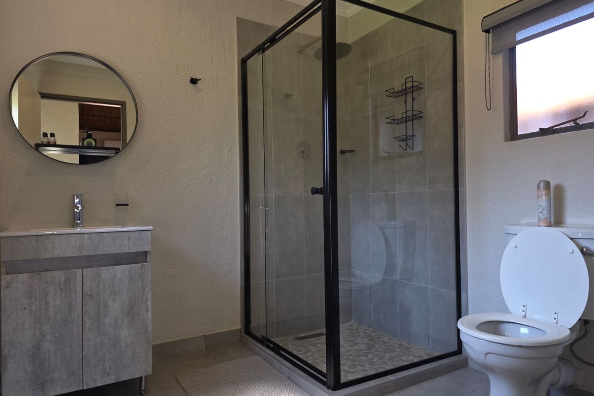 Modern bathroom featuring a vanity with basin, a glass-enclosed shower with pebble-style floor tiling, and a standard toilet.