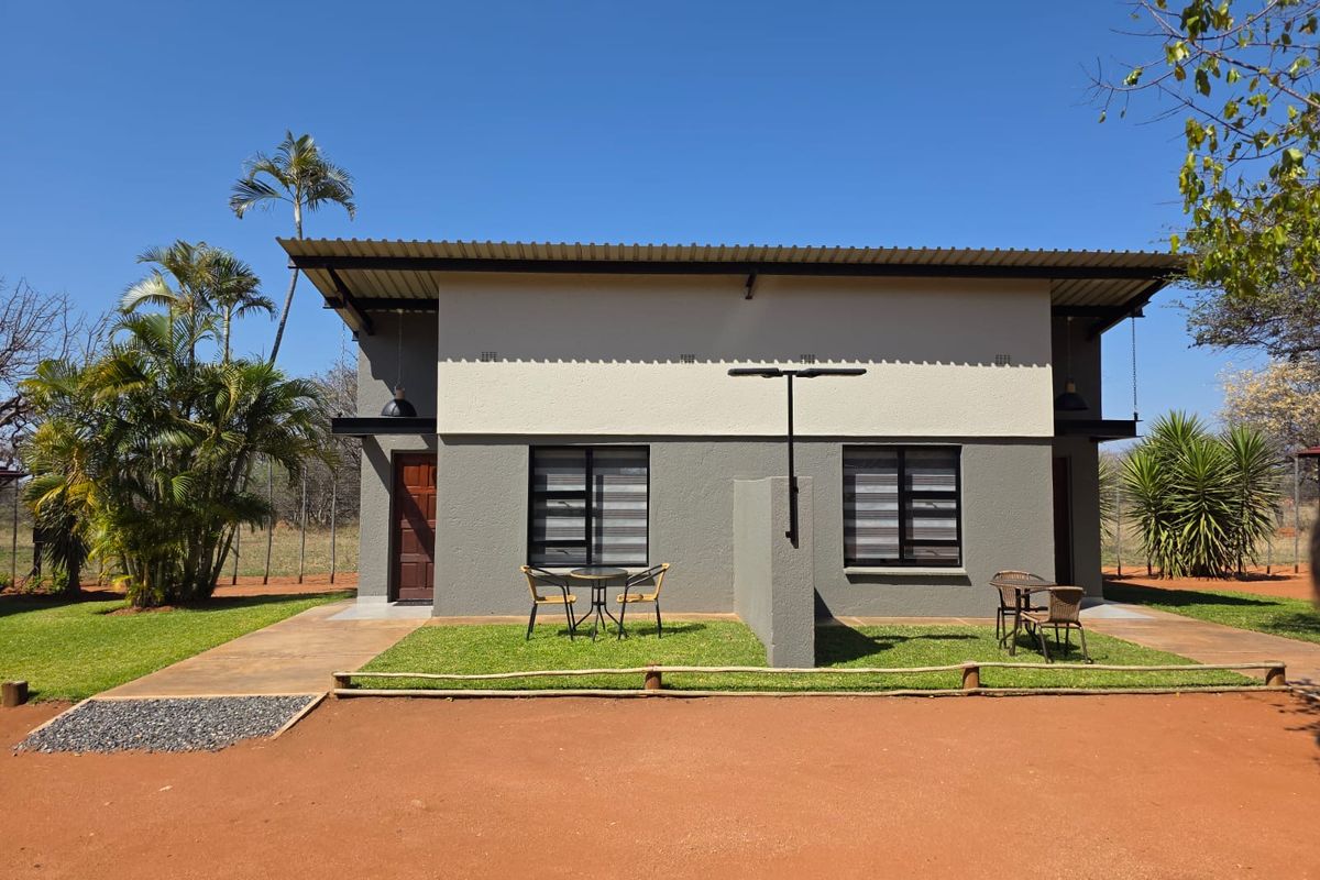 Rear view of a modern farm-style dwelling featuring a corrugated metal roof, concrete patio areas, and well-maintained garden surroundings.