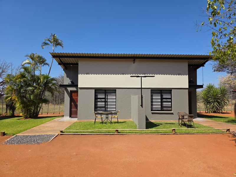 Rear view of a modern farm-style dwelling featuring a corrugated metal roof, concrete patio areas, and well-maintained garden surroundings.