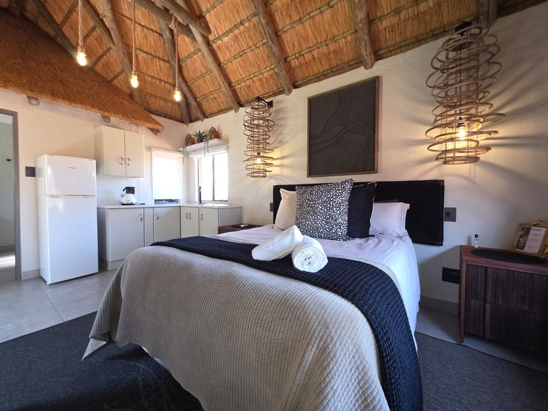 A charming open-plan bedroom featuring a high thatched roof with exposed timber rafters, integrated kitchen cabinetry, and modern finishes.