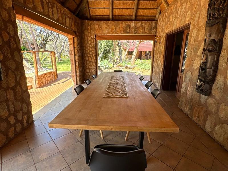 Spacious covered outdoor dining area featuring rustic stone walls, a traditional thatched roof, and tiled flooring, opening directly onto the garden.