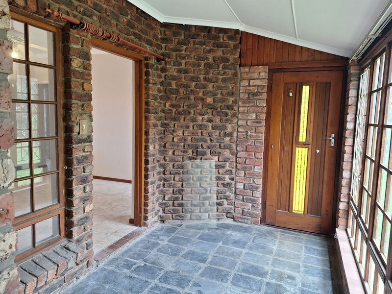 A covered patio area featuring exposed brick walls, slate flooring, and timber-framed windows, providing a rustic transition space to the interior.
