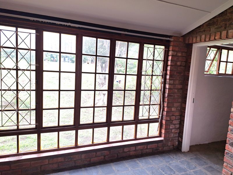 A sunroom or enclosed patio featuring exposed brick walls, slate flooring, and large timber-framed windows overlooking the garden.