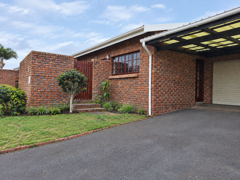Front elevation of a face brick townhouse featuring a paved driveway, integrated carport with a roller door, and a private gated entrance.