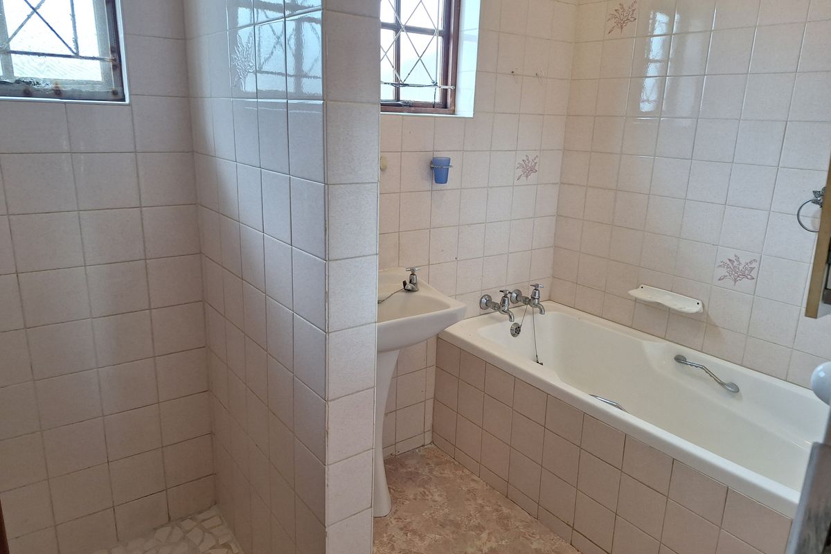 A dated bathroom featuring a pedestal basin, bathtub, and separate shower enclosure with tiled walls and security bars on the windows.