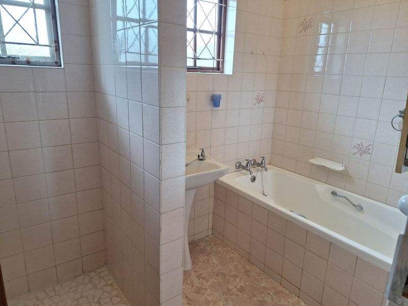 A dated bathroom featuring a pedestal basin, bathtub, and separate shower enclosure with tiled walls and security bars on the windows.