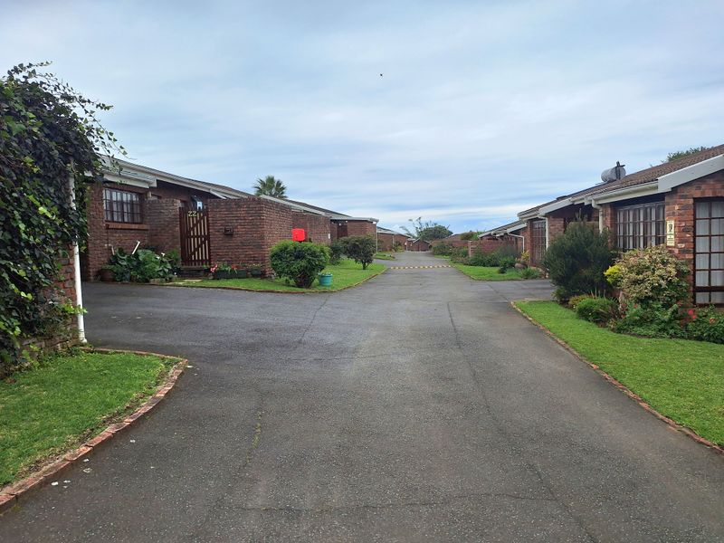 A view of the complex driveway and brick townhouse facades with established landscaping and paved access.