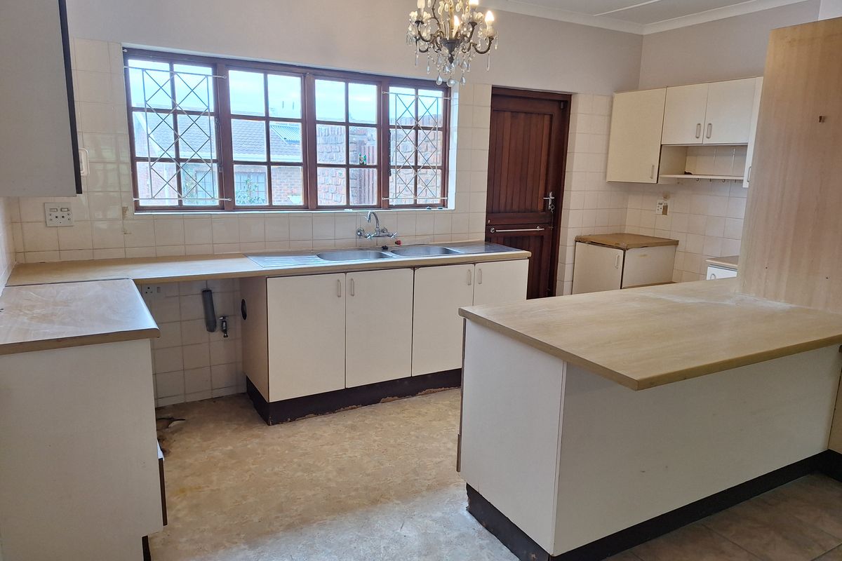 A spacious kitchen featuring built-in cabinetry, laminate countertops, and a double basin sink, currently awaiting new flooring and modern updates.