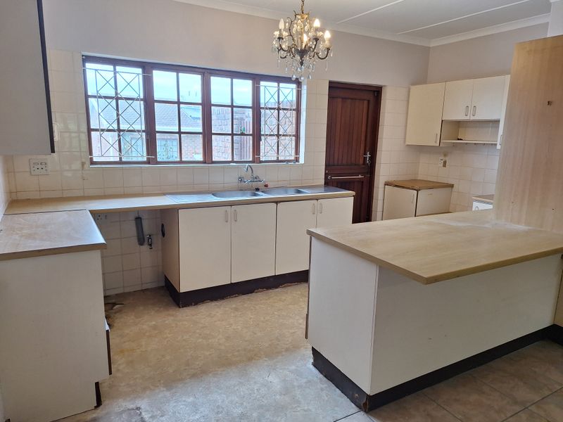 A spacious kitchen featuring built-in cabinetry, laminate countertops, and a double basin sink, currently awaiting new flooring and modern updates.