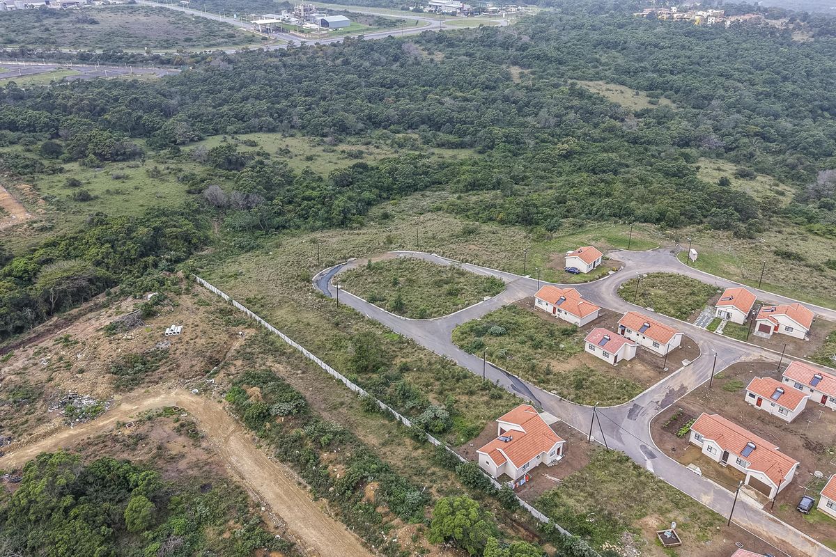Aerial view of a residential development featuring paved roads, street lighting, and multiple detached homes set within a natural landscape.