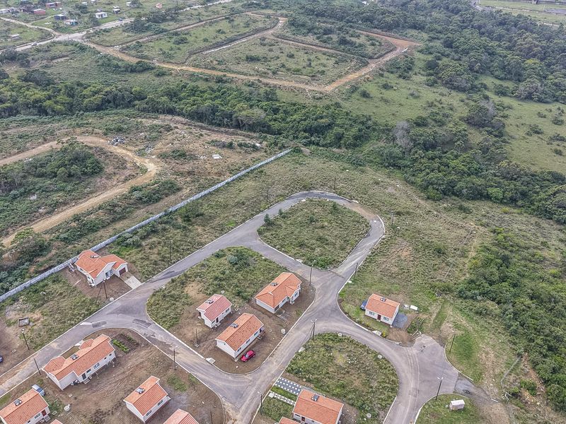 Aerial view of a residential development featuring established paved roads, street lighting, and multiple detached homes set within a natural landscape.
