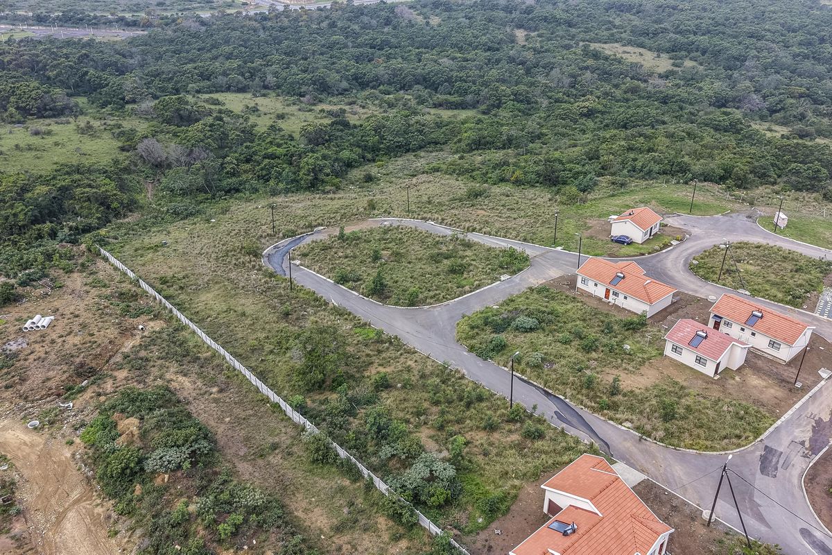 Aerial view of a residential development site featuring paved roads, street lighting, and perimeter fencing, surrounded by natural vegetation.
