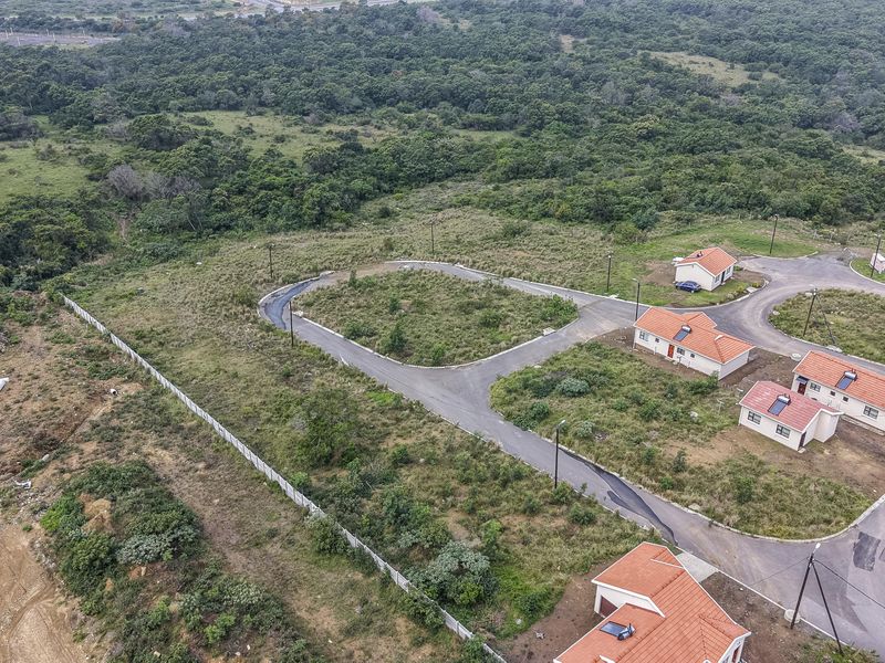 Aerial view of a residential development site featuring paved roads, street lighting, and perimeter fencing, surrounded by natural vegetation.