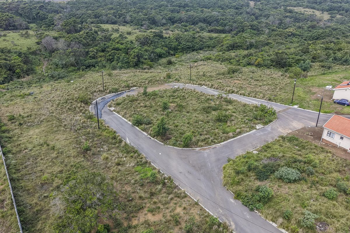 Aerial view of a vacant residential plot featuring a paved cul-de-sac, established street lighting, and surrounding natural vegetation.