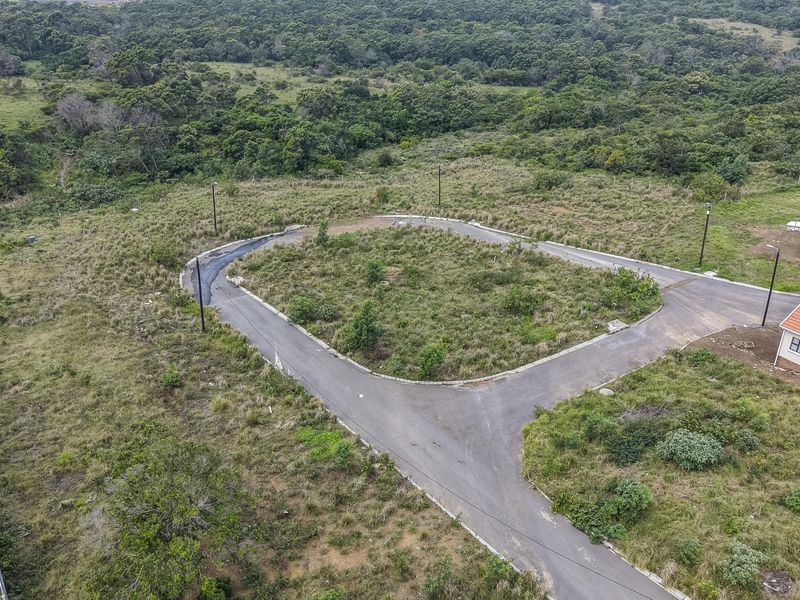 Aerial view of a vacant residential plot featuring a paved cul-de-sac, established street lighting, and surrounding natural vegetation.