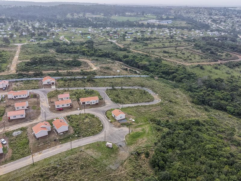 Aerial view of a residential development featuring multiple detached homes, paved internal roads, and surrounding natural landscape.