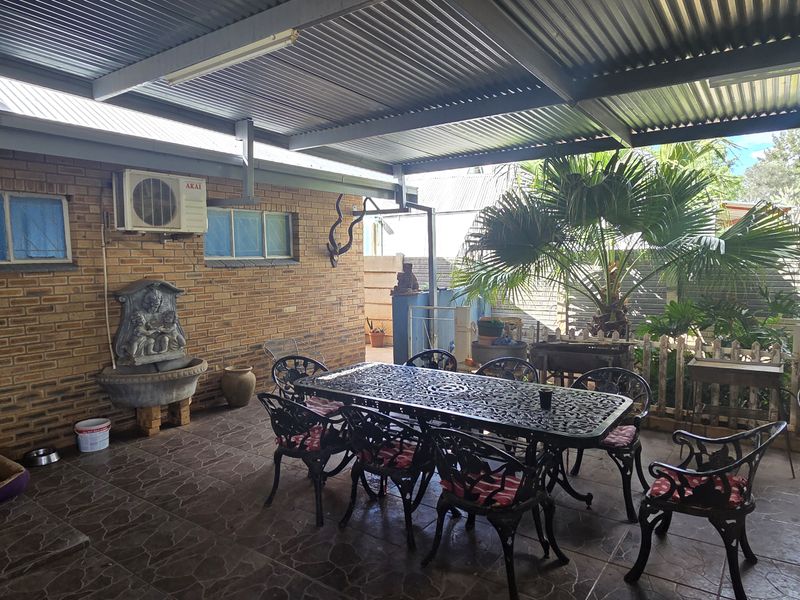 A covered outdoor patio area featuring brick walls, tiled flooring, a corrugated metal roof, and a built-in wall fountain, providing a functional space for entertaining.