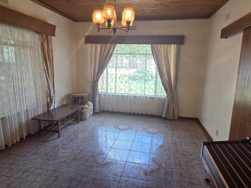 A spacious living room featuring timber ceilings, tiled flooring, and large windows that provide ample natural light.