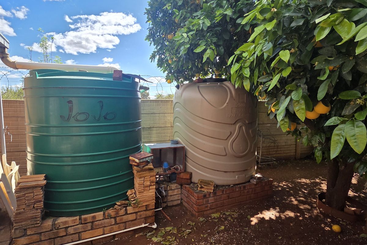 Rear exterior area featuring two large water storage tanks mounted on brick stands, adjacent to a brick building wall and mature citrus trees.