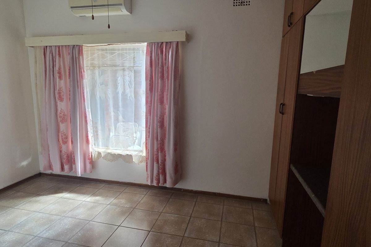 A functional bedroom featuring tiled flooring, built-in wooden cupboards, and an air conditioning unit, offering a blank canvas for potential updates.