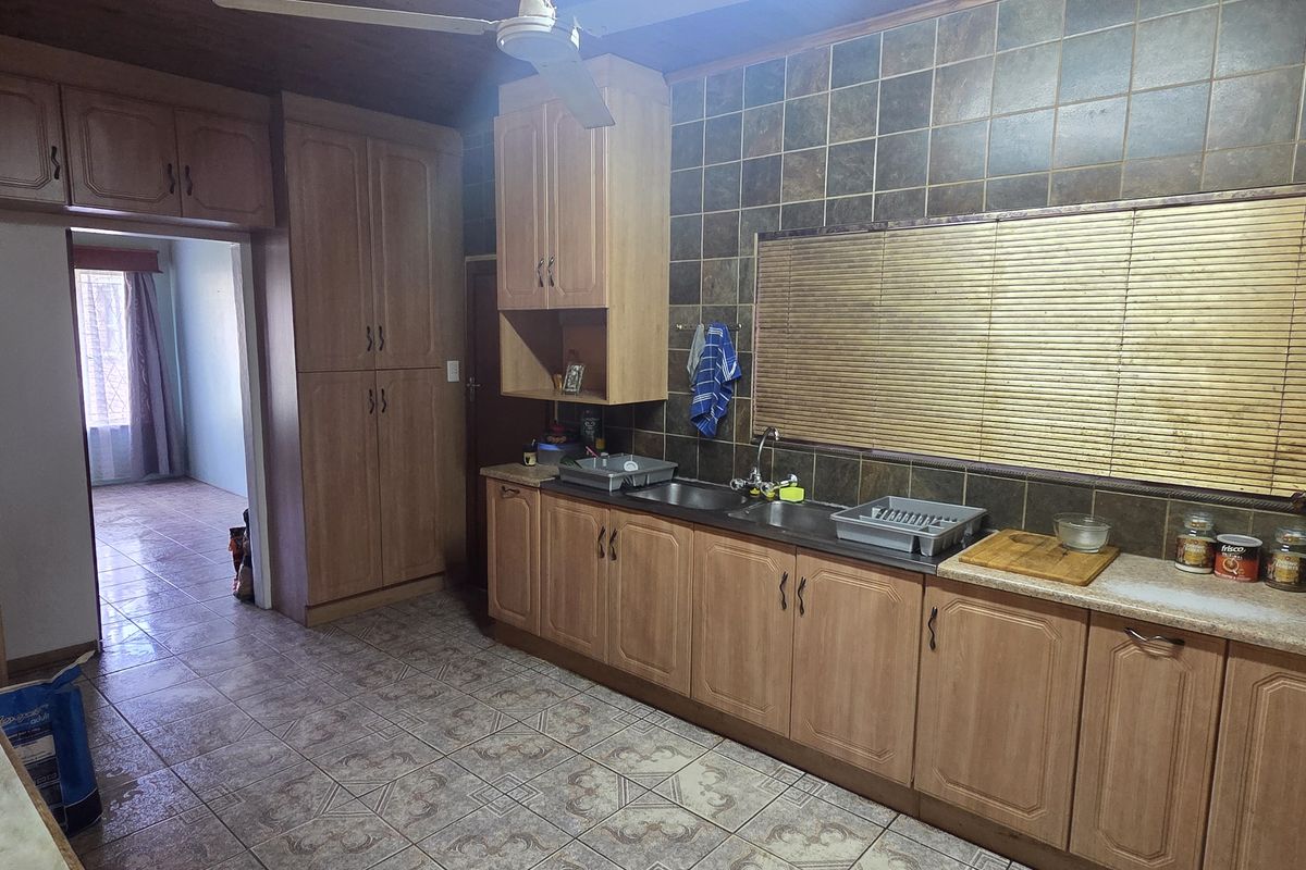 A functional kitchen featuring wood-look cabinetry, a double basin sink, and tiled splashbacks, offering a practical layout with potential for modern updates.