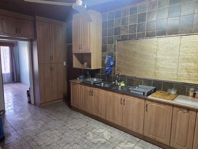 A functional kitchen featuring wood-look cabinetry, a double basin sink, and tiled splashbacks, offering a practical layout with potential for modern updates.